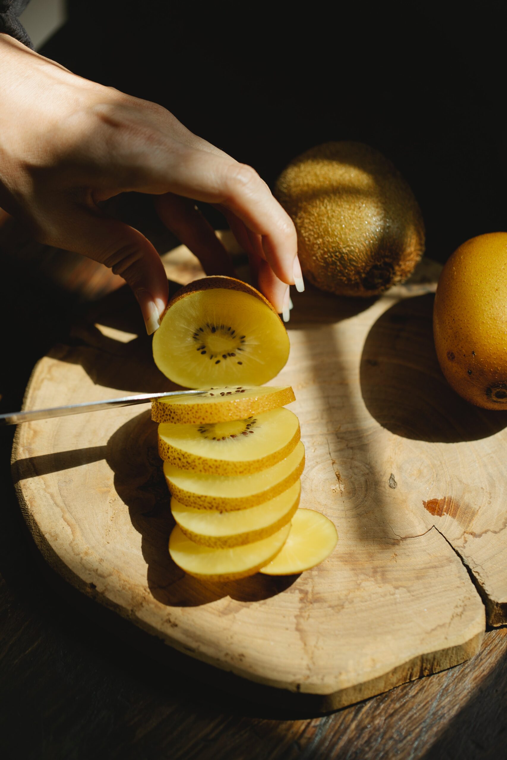 A hand finely slicing a kiwi on a wooden table
